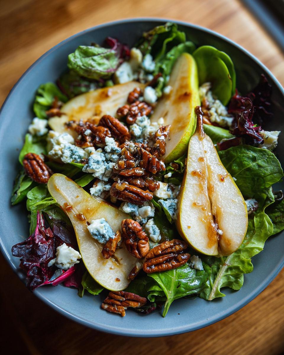 A close-up of a fresh pear salad with sliced pears, crumbled blue cheese, and candied pecans on a bed of mixed greens.