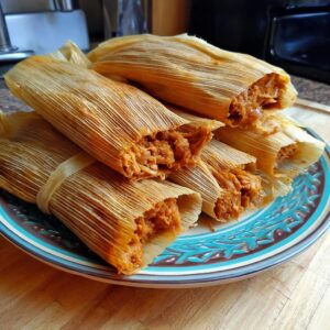 A close-up of several tender pork tamales, unwrapped to reveal the savory filling, served on a decorative plate.