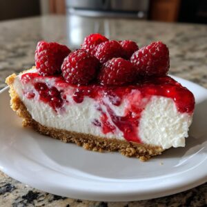 A perfect slice of creamy raspberry cheesecake topped with fresh raspberries and raspberry sauce on a white plate.