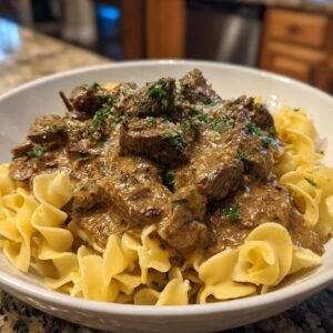 A close-up of a bowl of tender Beef Stroganoff served over wide egg noodles, garnished with parsley and cheese.