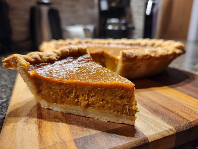 A close-up of a slice of vegan pumpkin pie on a wooden cutting board, showcasing its creamy texture and golden crust.